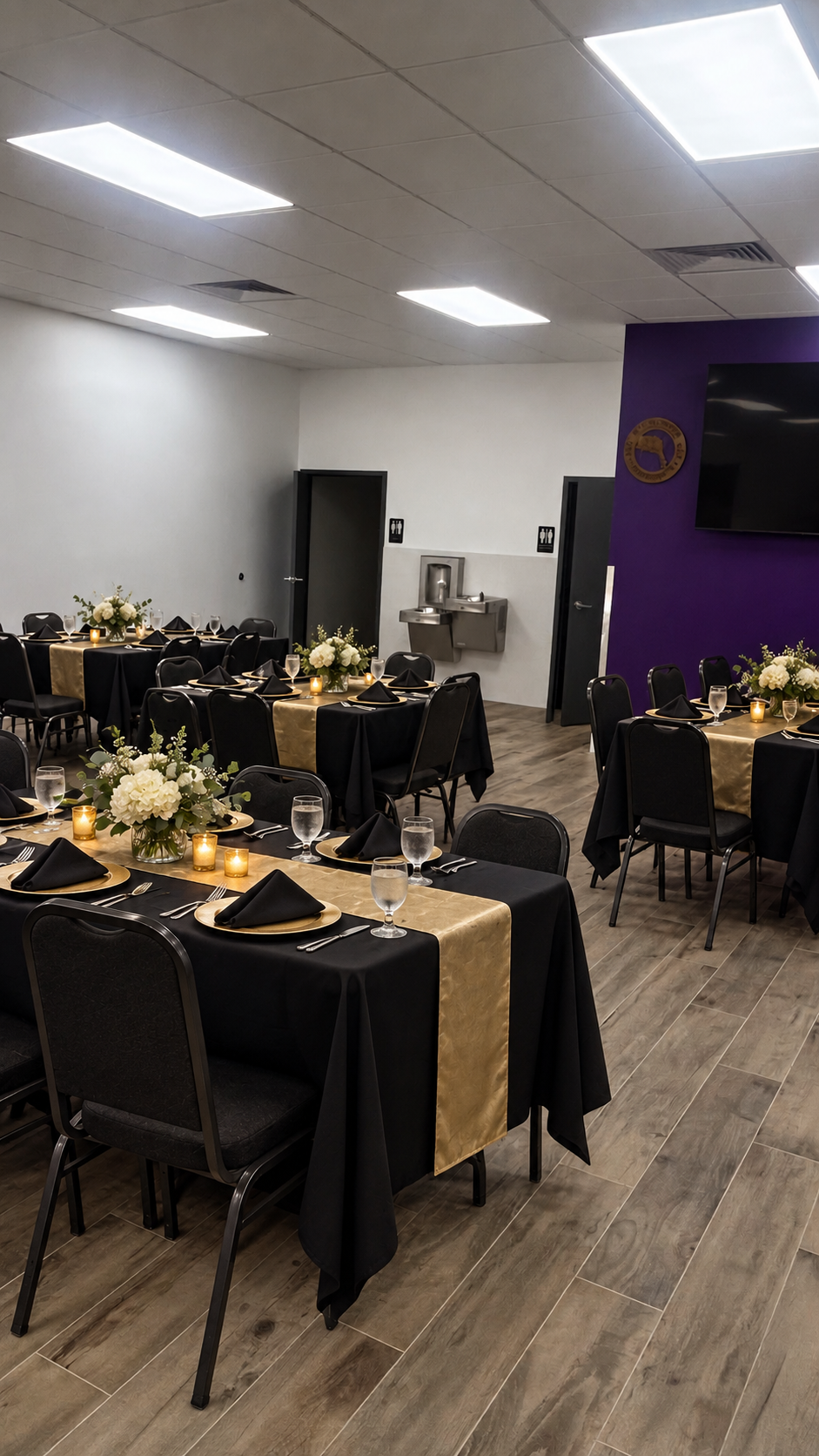 Same main hall dressed for a formal dinner — black and gold table settings beneath the purple accent wall