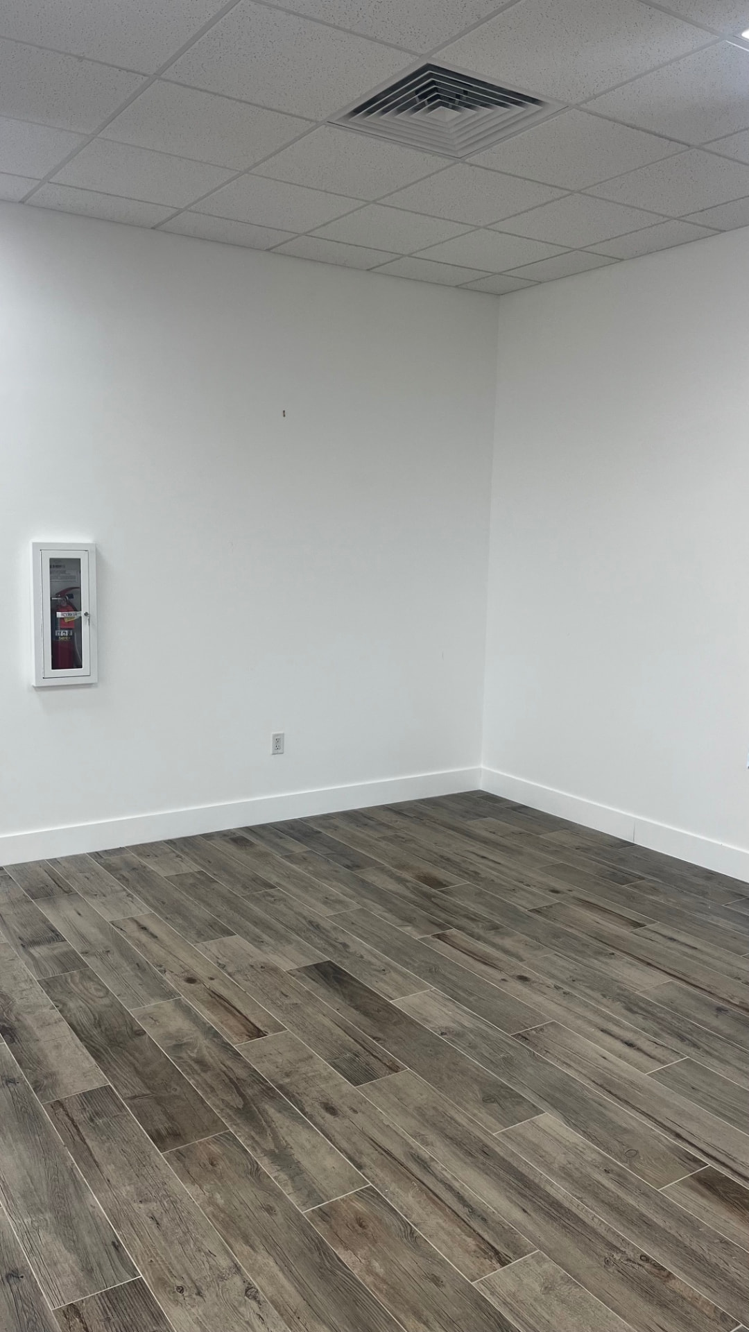Open event space empty — corner with wood-look flooring, ceiling vent and fire extinguisher cabinet